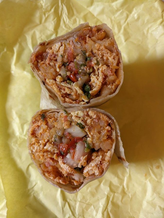 Breakfast burrito cut in half on yellow wrap paper, showing eggs, potatoes, and house-made pico de gallo