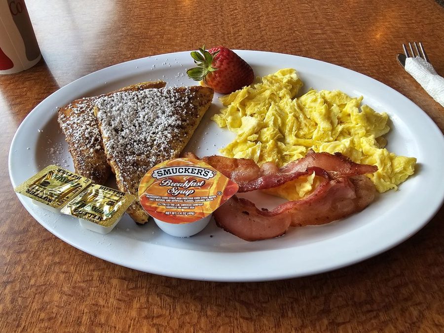 French toast breakfast plate with scrambled eggs, bacon, and a strawberry