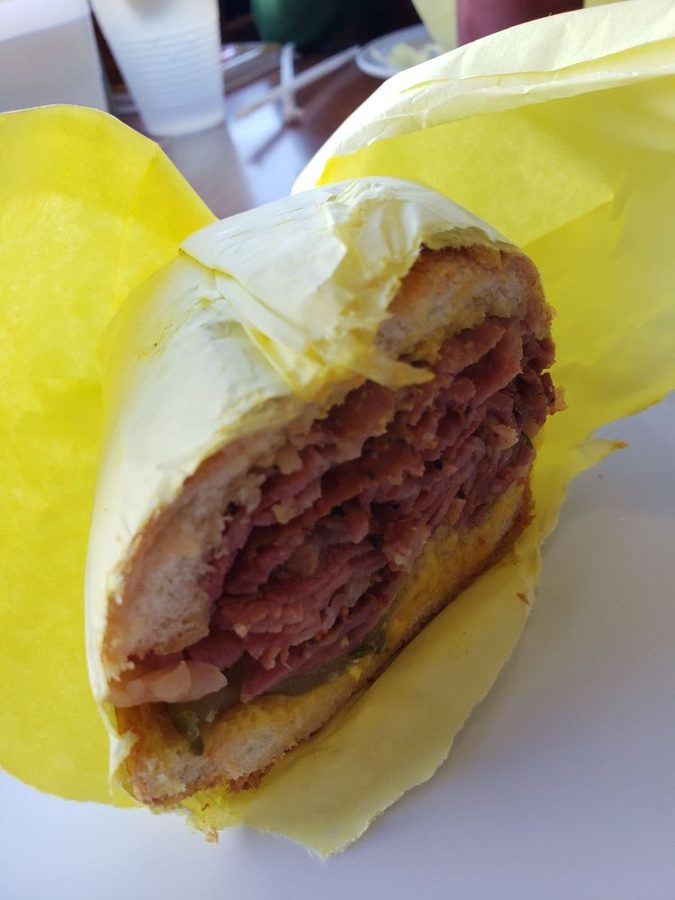 Pastrami sandwich stacked high, half-wrapped in yellow paper