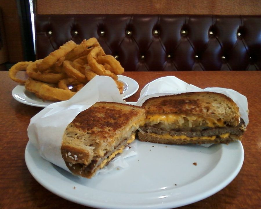 Patty melt cut in half with a plate of onion rings, in front of a tufted booth